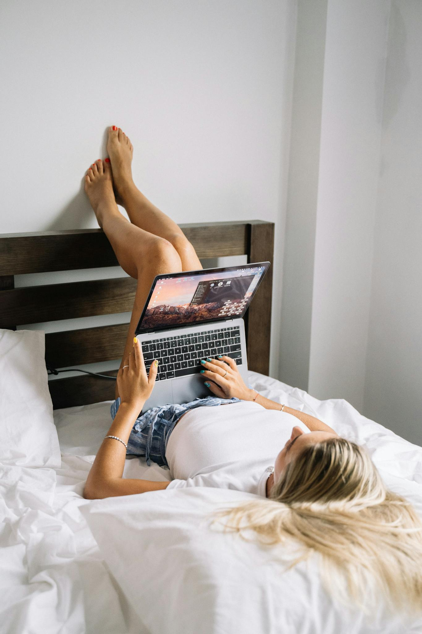 About Young woman lying in bed, using a laptop, relaxing in a cozy bedroom setting.